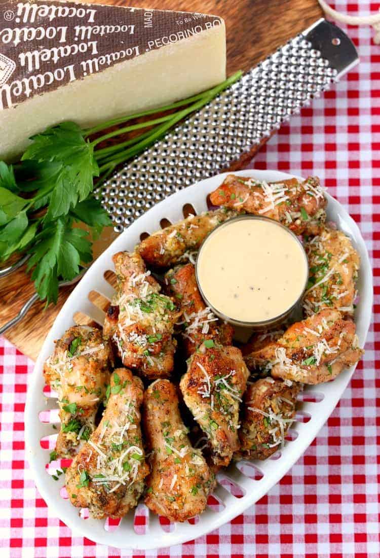 A bird's eye view of a plate of Baked Garlic Parmesan Chicken Wings with a cup of caesar dressing in the middle.