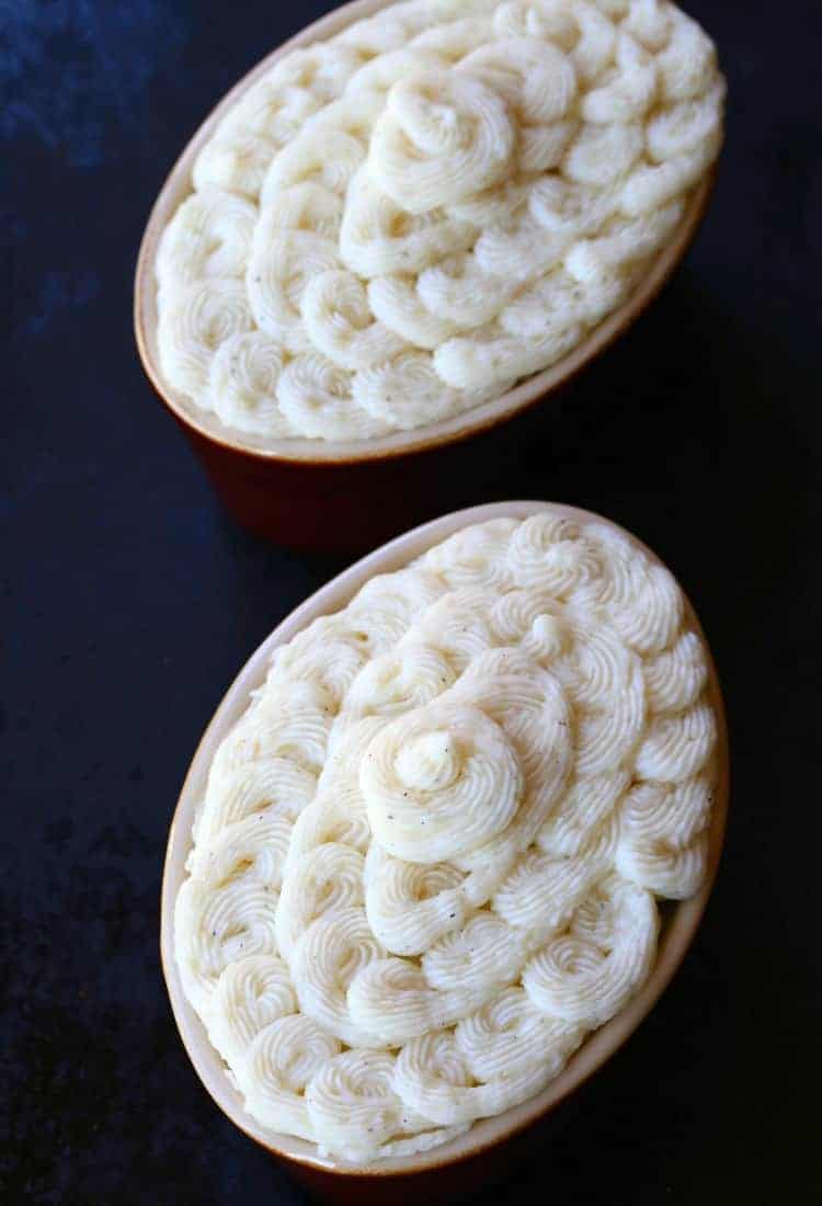 Overhead view of two uncooked turkey shepherd's pies, with piped mashed potatoes on top