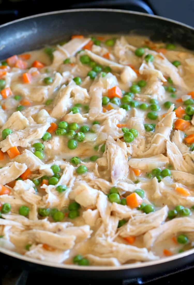 A pot filled with the filling for turkey shepherd's pie: peas, carrots, shredded turkey, and gravy sauce