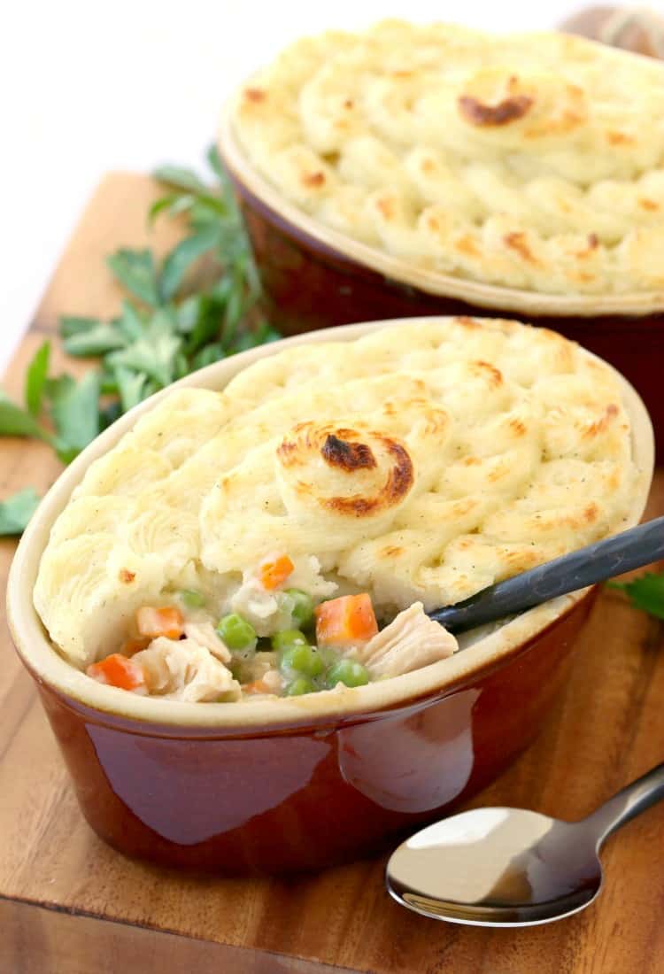 A casserole dish with turkey shepherd's pie, with a serving removed and a serving spoon in it, next to another casserole dish of shepherd's pie