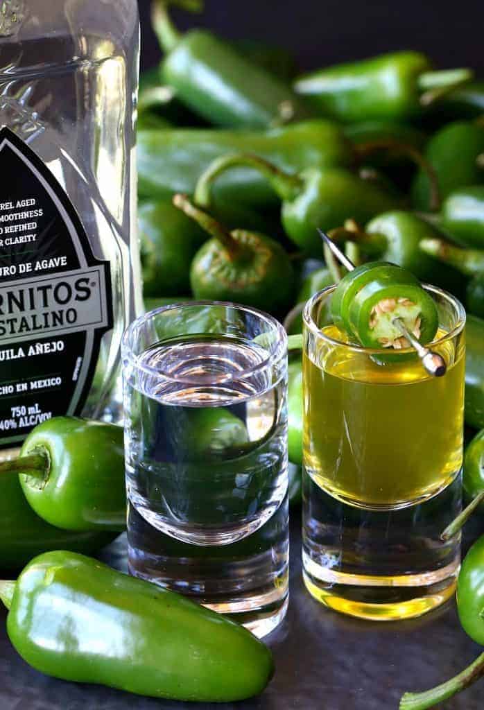 A shot glass full of tequila next to a second shot glass full of jalapeño brine with two jalapeño slices as garnish.