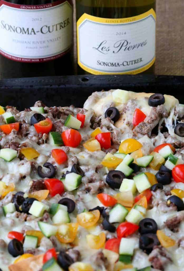 greek nachos on a baking sheet with wine bottle