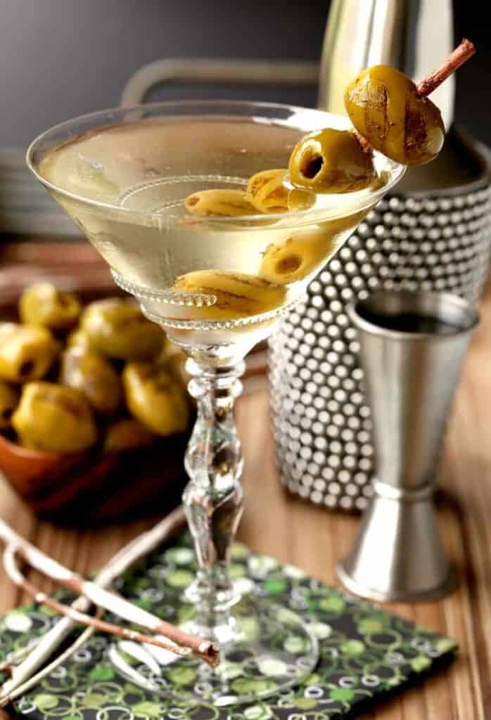 Grilled Dirty Martini in glass with shaker and olives and cocktail napkin