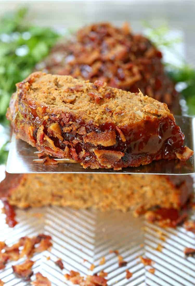 A slice of turkey meatloaf on a spatula, held up in the air, with the rest of the meatloaf in the background