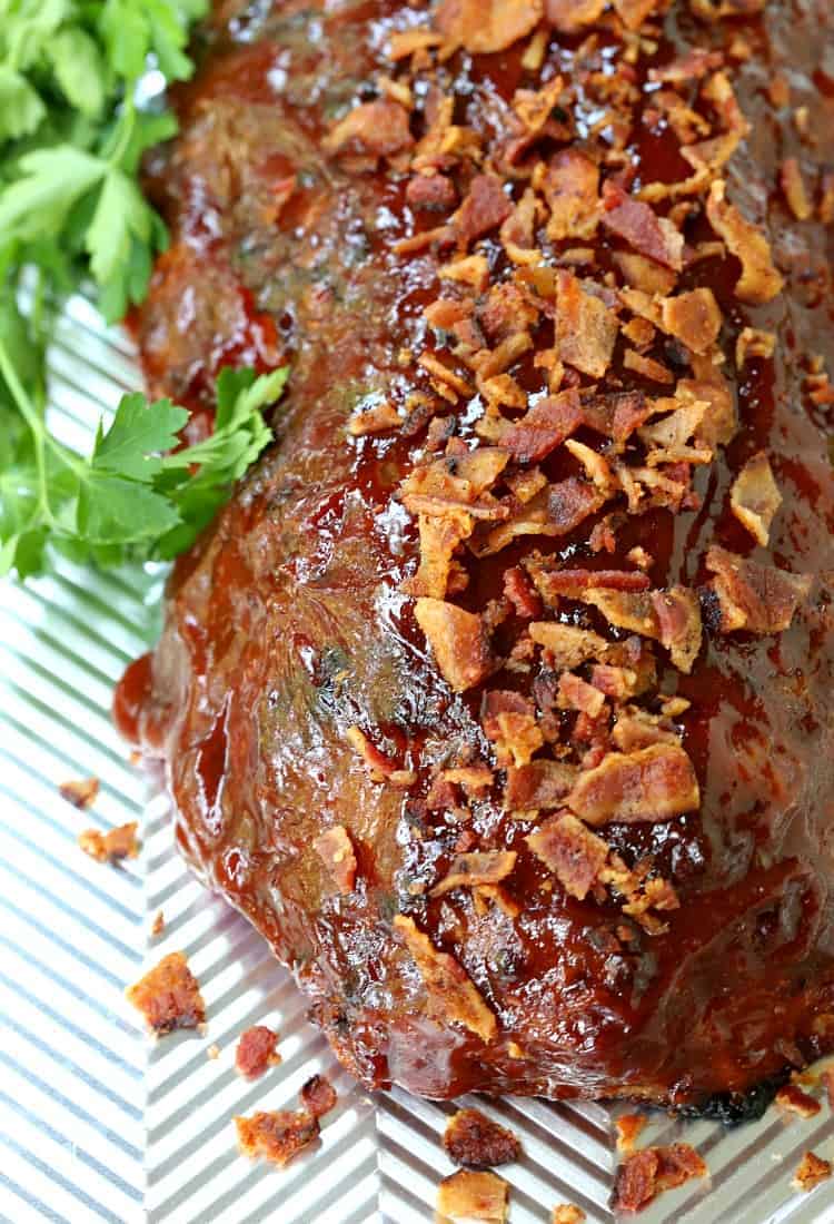 Close up of a turkey meatloaf topped with crumbled bacon, next to a sprig of parsley