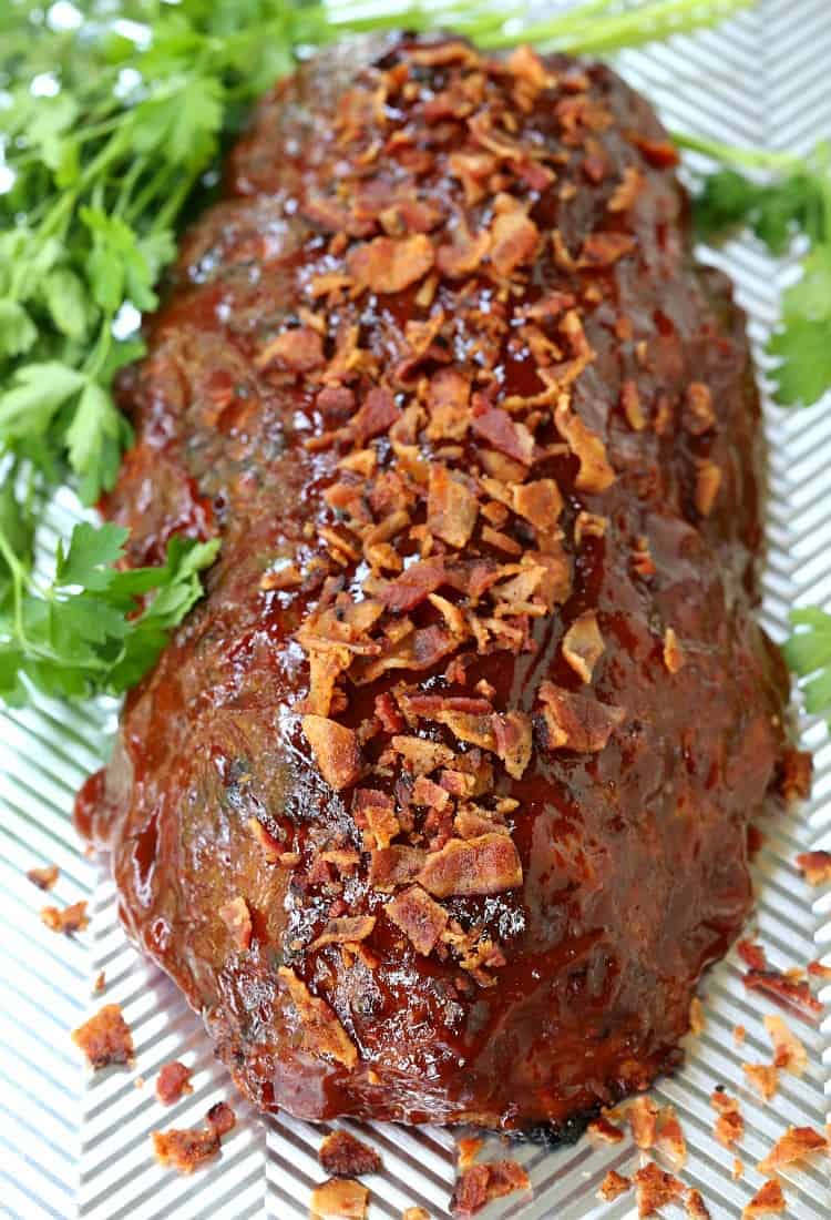 A whole turkey meatloaf, covered in crumbled bacon, surrounded by sprigs of parsley