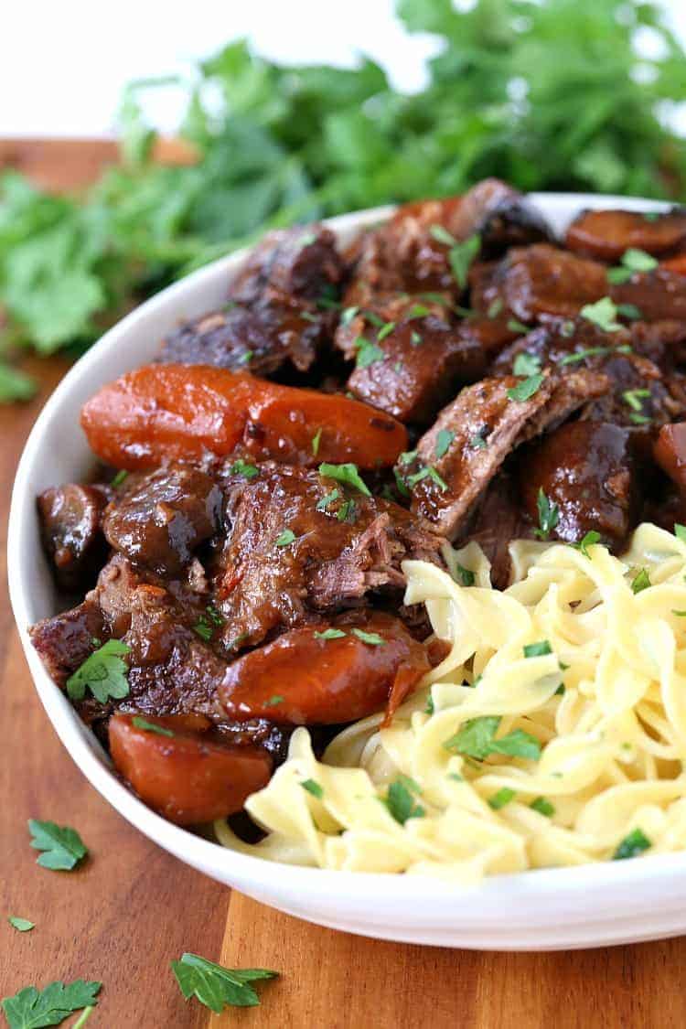 French Bistro Beef Stew in a bowl with noodles on a board