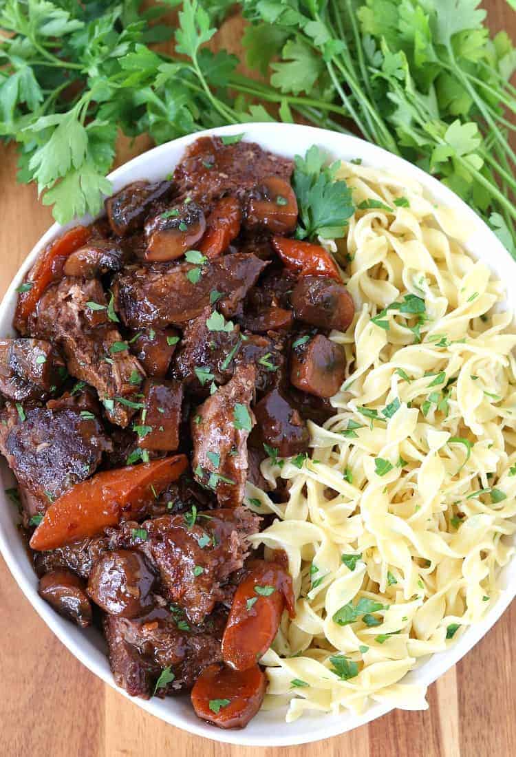 French Bistro Beef Stew in a bowl with noodles on a board