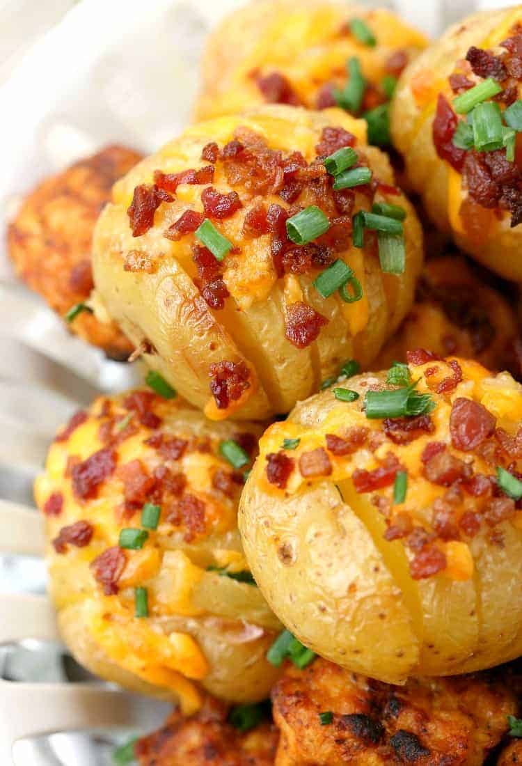 A stack of mini hasselback potatoes with melty cheese, bacon bits, and chives on top