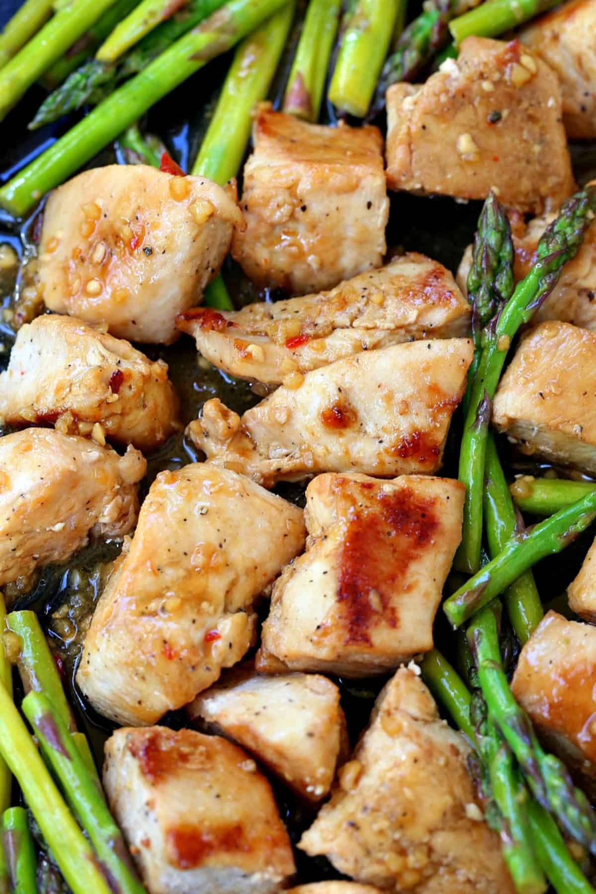 pieces of marinated chicken with asparagus on a sheet pan
