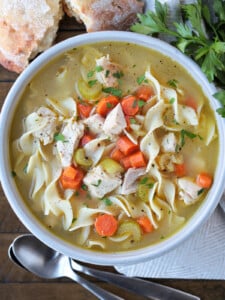 turkey soup with noodles in a bowl with spoons and bread