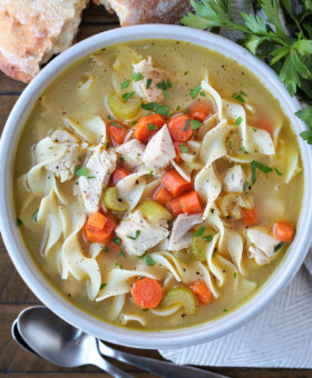 turkey soup with noodles in a bowl with spoons and bread