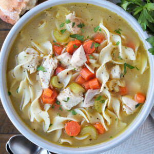 turkey soup with noodles in a bowl with spoons and bread