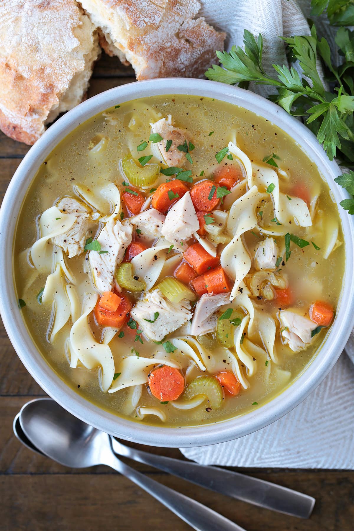turkey soup with noodles in a bowl with spoons and bread
