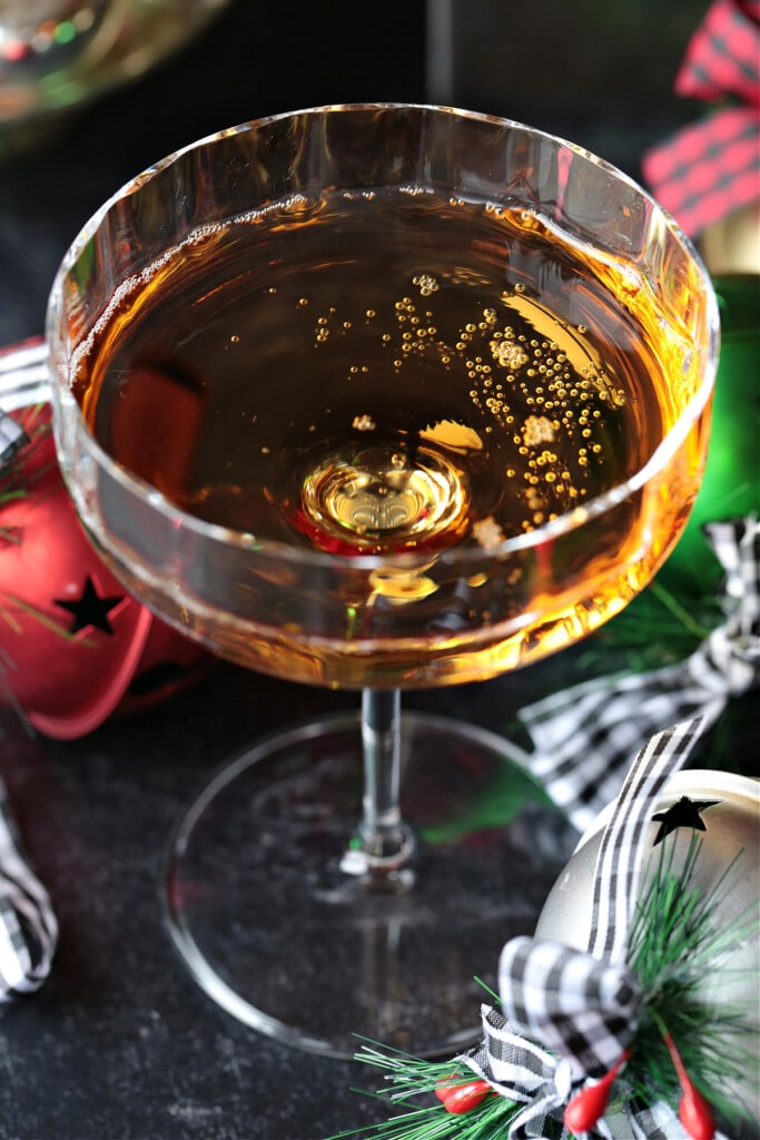 This Christmas Mimosa Recipe is perfect for your holiday parties and brunches! A beautiful, layered cocktail that tastes as good as it looks! champagne in a wide glass with Christmas decorations