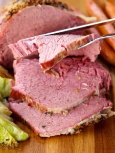 Sliced Crock Pot Corned Beef on a wooden cutting board next to braised cabbage and carrots.