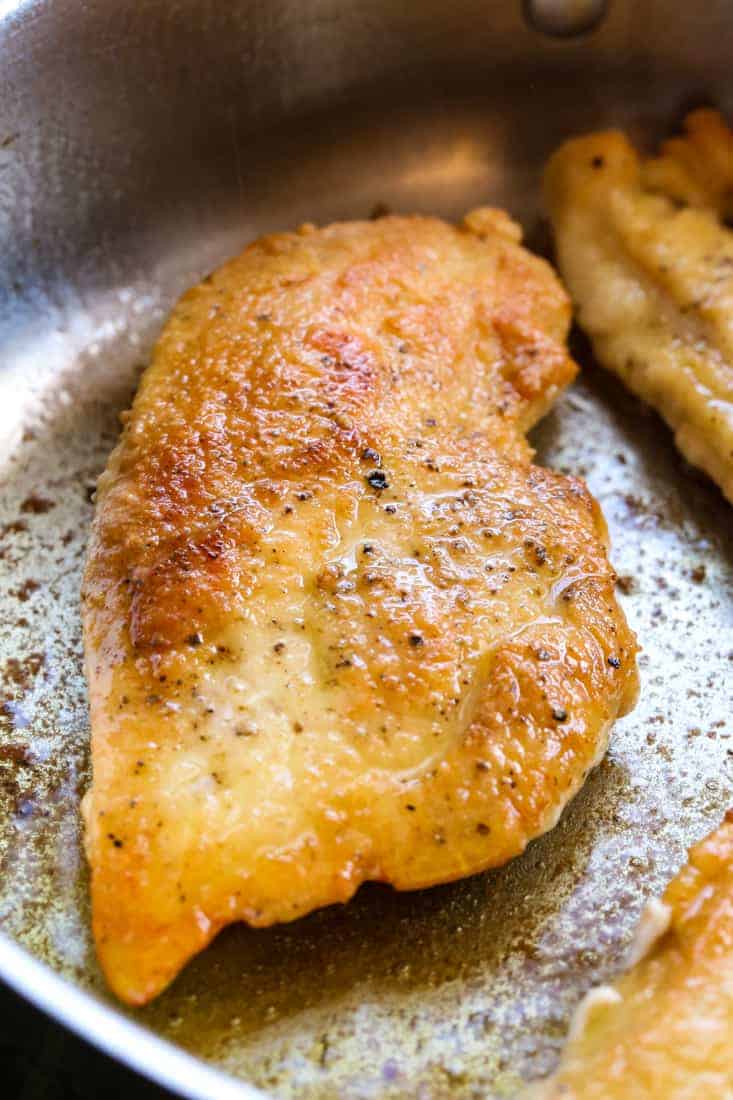 A seasoned chicken breast being cooked in a pan