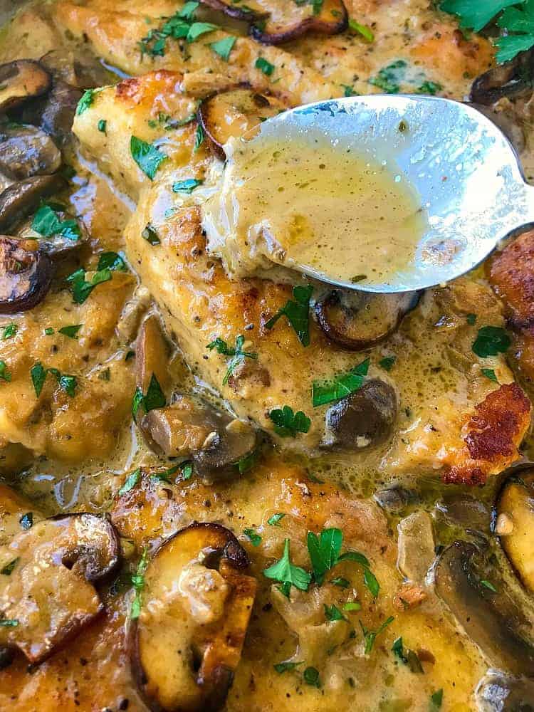 A spoon pouring marsala sauce over a piece of chicken and mushrooms