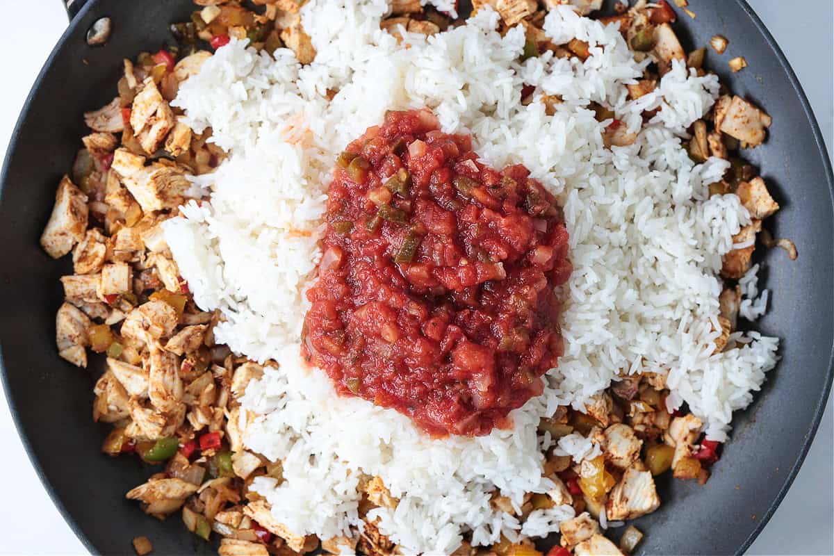 Chicken Fajita Rice is packed with charred vegetables, tender chicken and seasoned rice. Ideal for busy nights, ready in less than 30 minutes! cooked white rice and salsa in a pan with chicken and vegetables