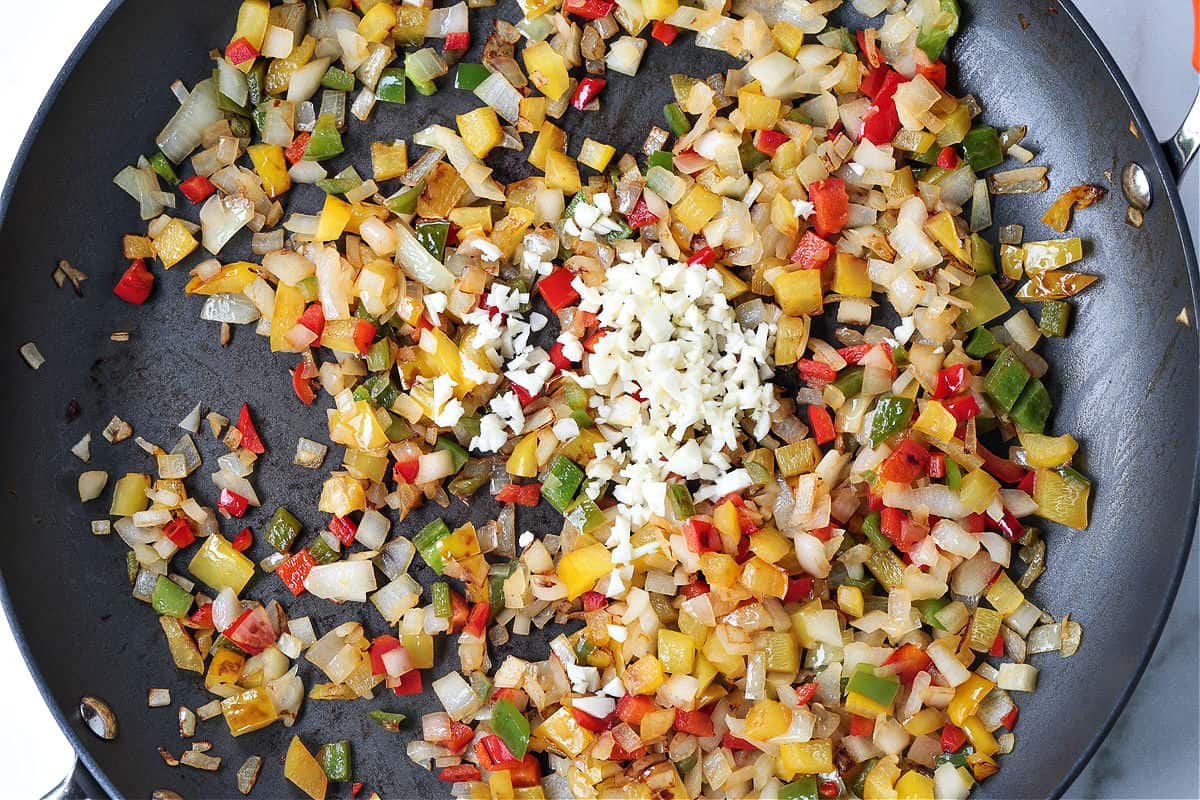 Chicken Fajita Rice is packed with charred vegetables, tender chicken and seasoned rice. Ideal for busy nights, ready in less than 30 minutes! peppers and onions in a skillet with garlic