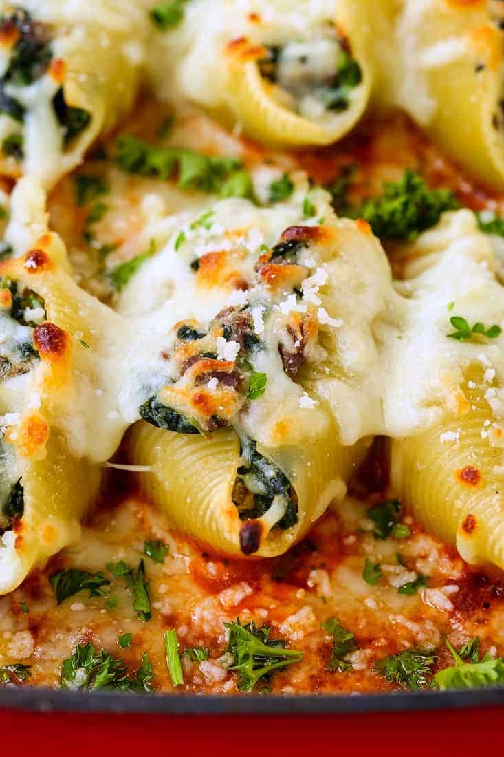 A stuffed shell from up close covered in toasty cheese and a garnish of parsley.