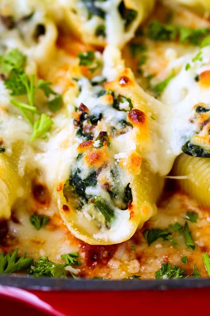 A close-up of a stuffed shell with meat, ricotta and spinach filling inside on a bed of tomato sauce.