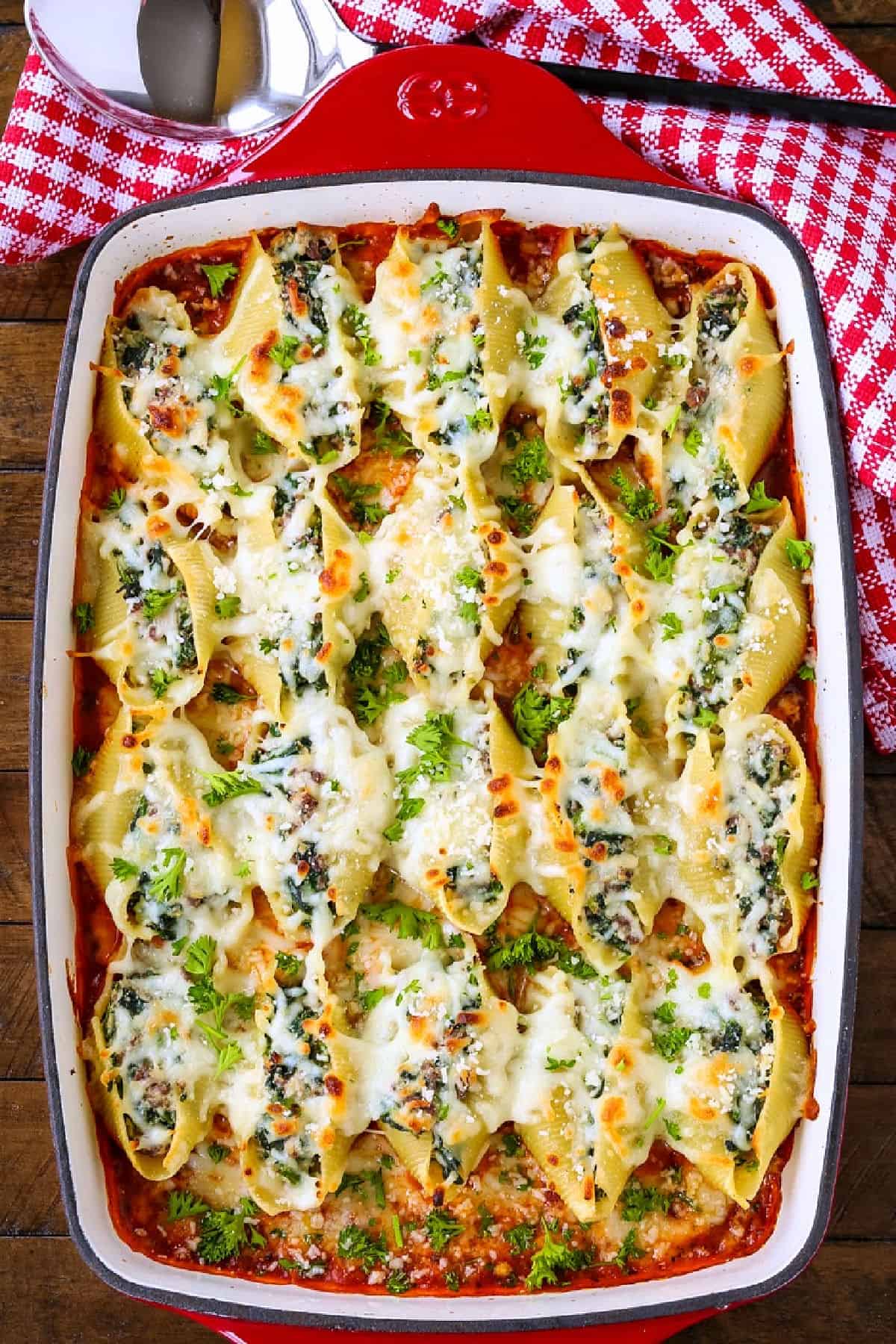 casserole dish with stuffed shells alongside of napkin and serving spoon