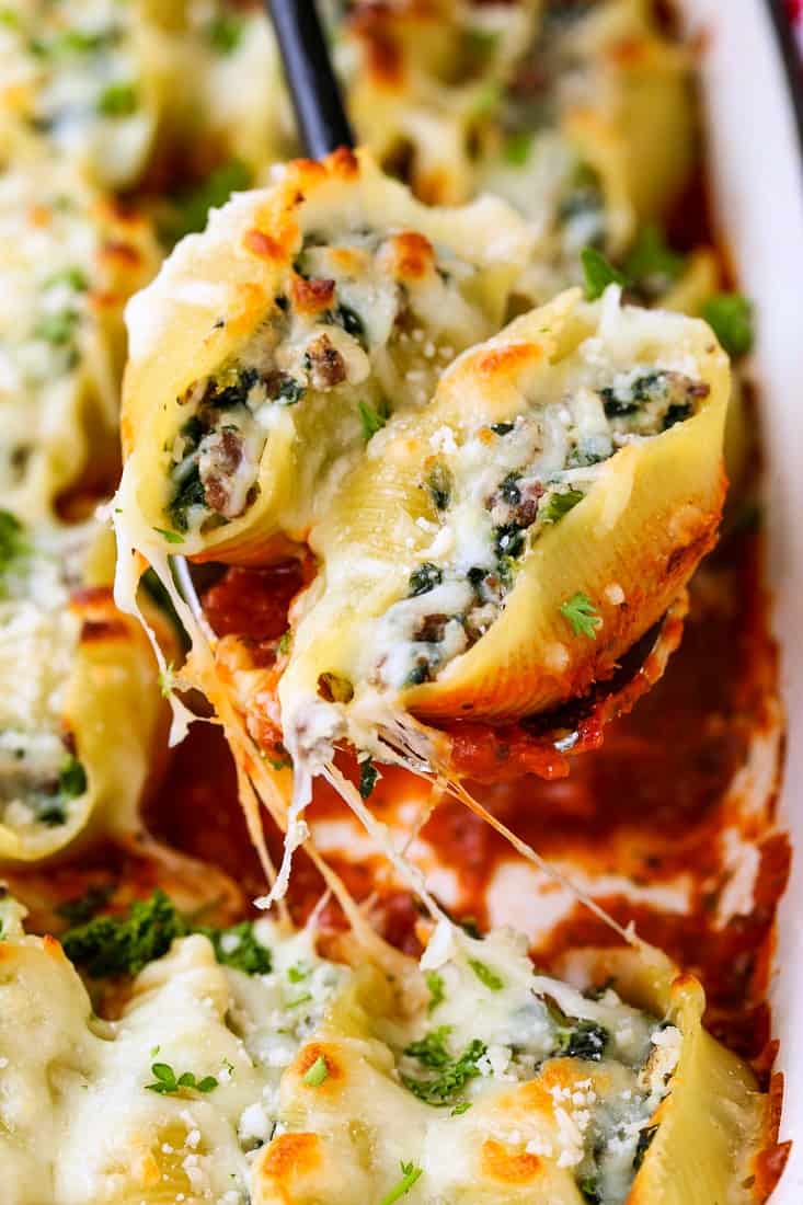 Two pasta shells stuffed with beefy ricotta and spinach filling being held toward the camera on a spoon.