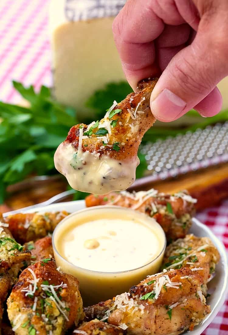Baked Garlic Parmesan Chicken Wings being dipped into caesar dressing