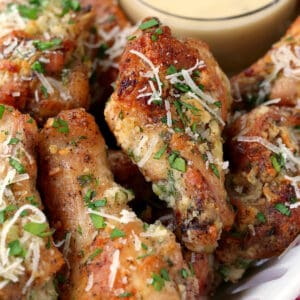 parmesan chicken wings stacked on a platter with sauce on the side
