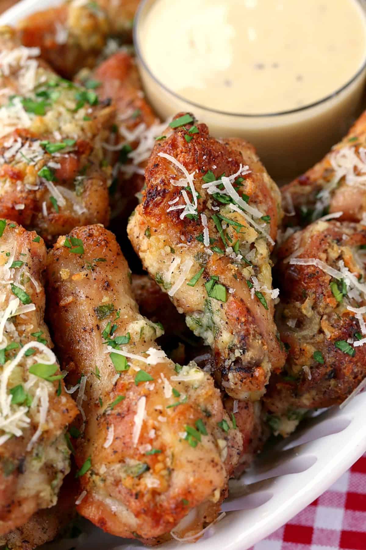 parmesan chicken wings stacked on a platter with sauce on the side