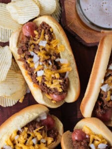 hot dogs with chili and cheese on a board with a beer