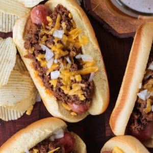 hot dogs with chili and cheese on a board with a beer