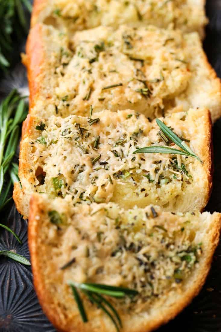 Rosemary Asiago Garlic Bread is herby and buttery with a crisp crust. Serve this garlic bread with everything from pasta to steak! Rosemary Asiago Garlic Bread sliced on a sheet pan