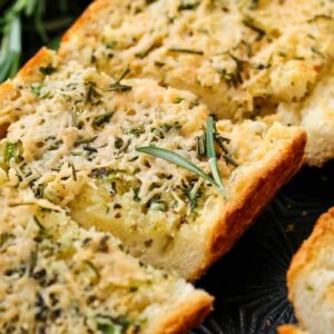 Rosemary Asiago Garlic Bread sliced on a baking sheet with rosemary garnish