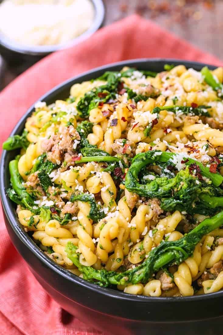 Pasta with Sausage and Broccolini in a black bowl with parmesan cheese on the side