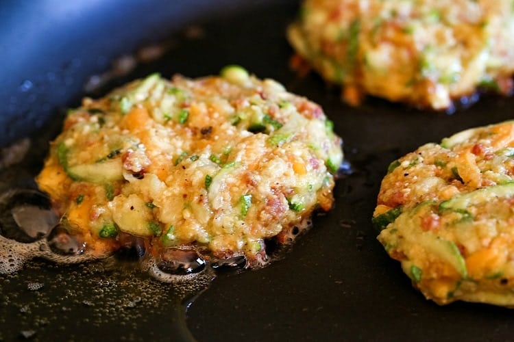 cheddar and bacon zucchini cakes frying in a skillet with oil