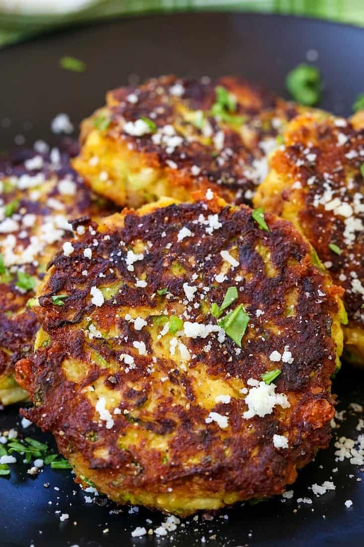zucchini cakes on a black plate with grated parmesan cheese and parsley