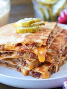 cheeseburger quesadillas stacked on a plate with cheese drip