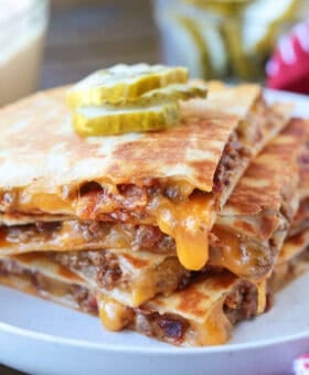 cheeseburger quesadillas stacked on a plate with cheese drip