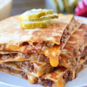 cheeseburger quesadillas stacked on a plate with cheese drip