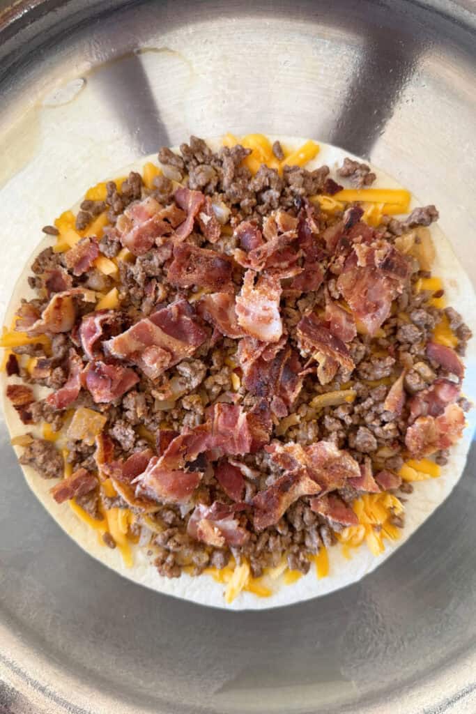 open quesadilla with cheese, beef filling and bacon in skillet