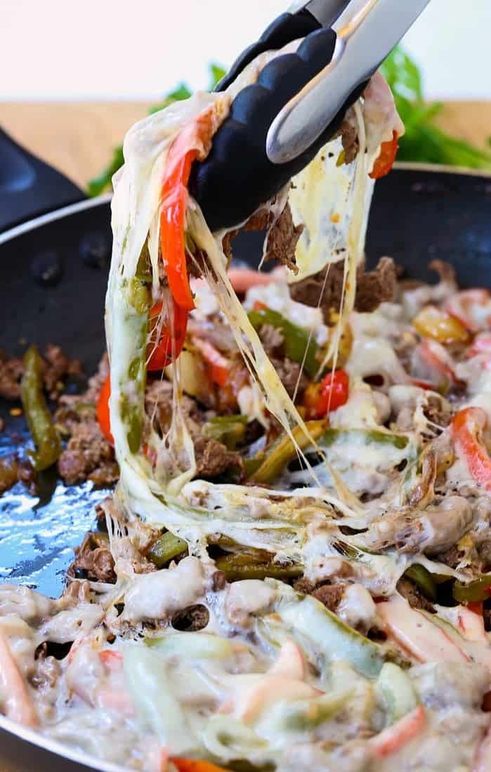 Quick Philly Cheesesteak Recipe in a skillet with tongs grabbing some of the beef and cheese