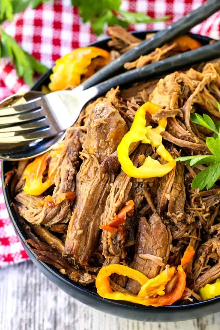 shredded beef in a bowl with peppers and forks on the side