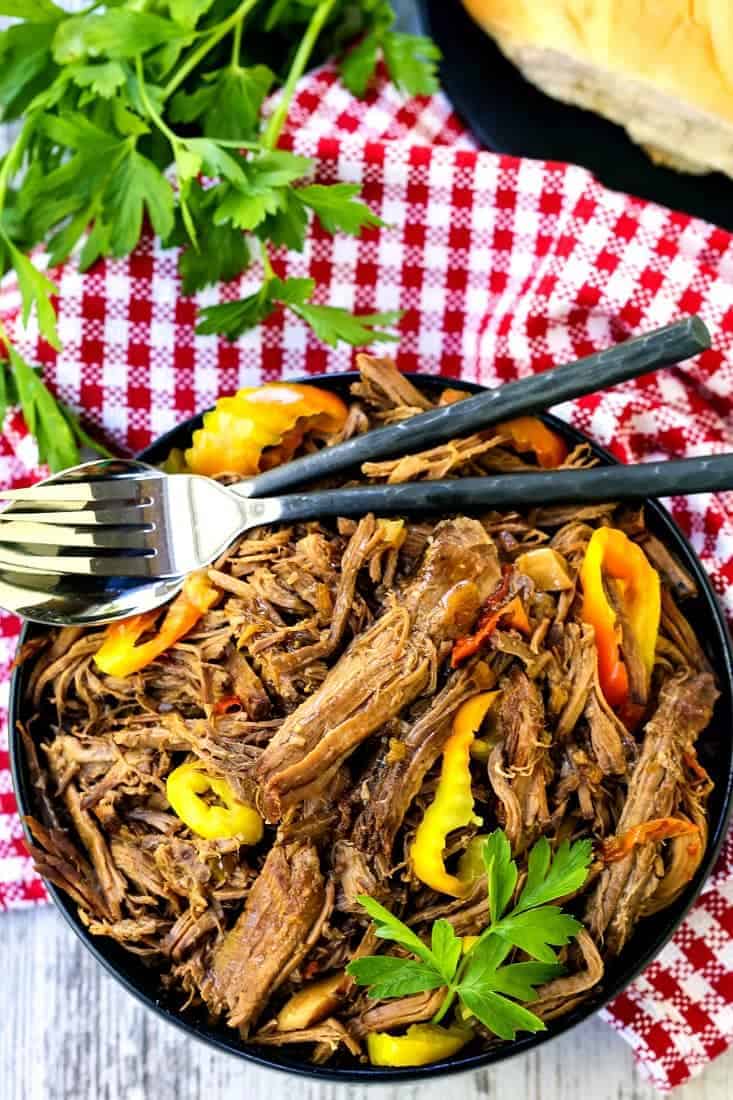 Pile this addicting Slow Cooker Italian Beef onto sub rolls, serve with mashed potatoes on the side or eat as is for a low carb meal! chuck roast shredded in a bowl with forks and a red and white napkin