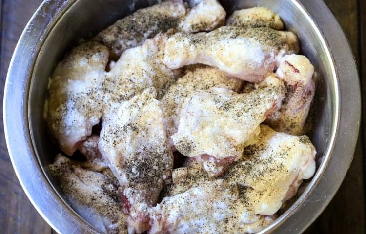 These Crispy Buffalo Chicken Wings are SO addicting and fall off the bone tender! A few tips make them as crispy as if you fried them! chicken wings in a bowl with seasonings