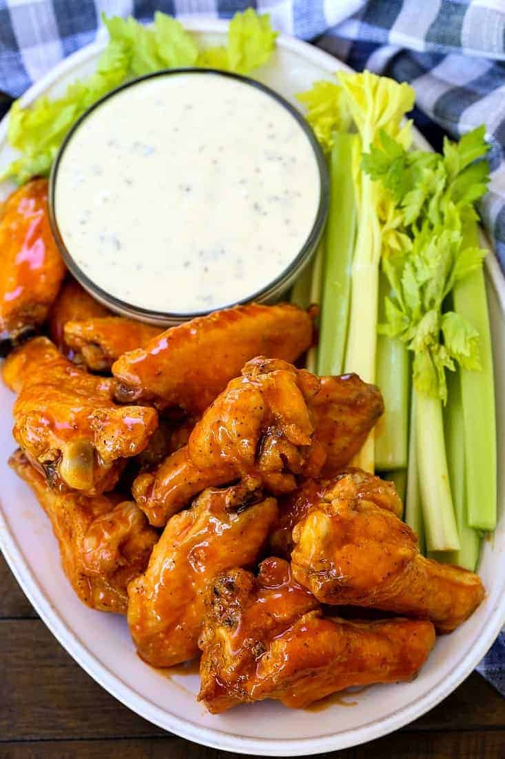 These Crispy Buffalo Chicken Wings are SO addicting and fall off the bone tender! A few tips make them as crispy as if you fried them! buffalo chicken wings on a platter with celery sticks and ranch