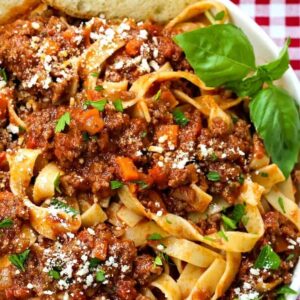 pasta with meat sauce in a white bowl with basil