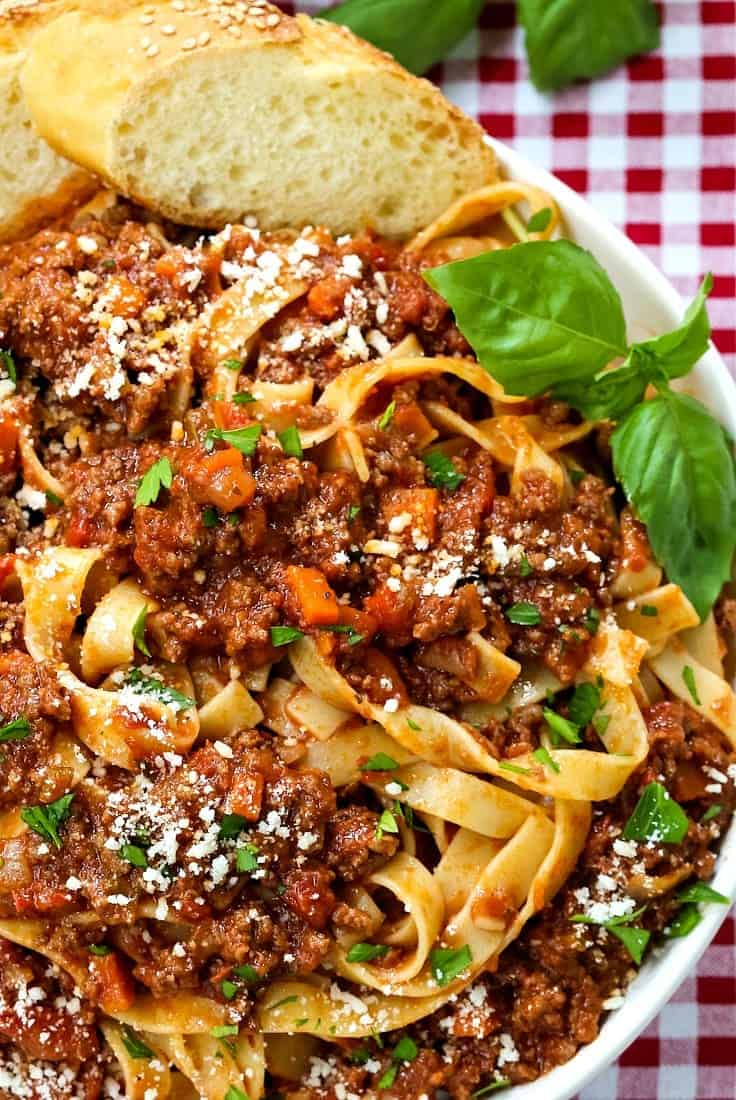 pasta with meat sauce in a white bowl with basil