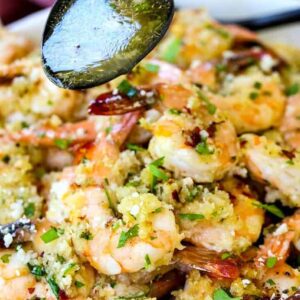 a spoon with sauce pouring over a bowl of shrimp